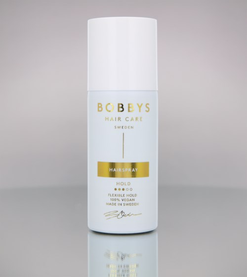 En vit burk med guldig och svart text, märkt som Bobbys Hair Care Sweden Hairspray, står på en enkel bakgrund.