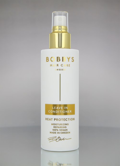 Eine weiße Flasche mit Goldkappe und gelbem Etikett, beschriftet 'Leave In Conditioner' für Haarpflege.