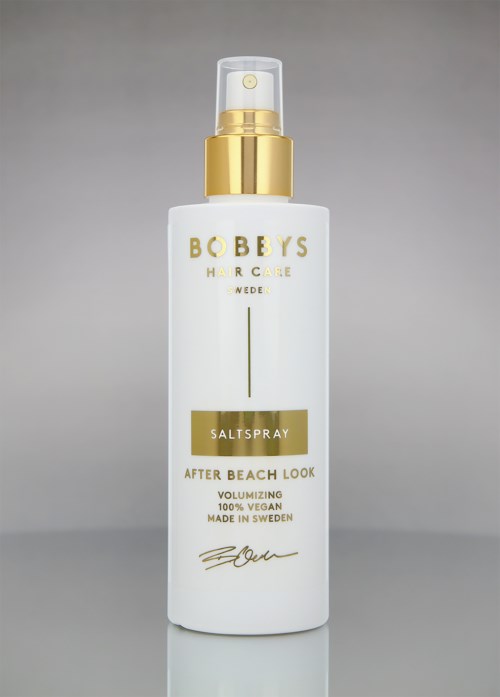 Eine weiße Flasche von Bobbys Salzspray für Haare mit Goldakzenten und Pumpe, für Beach-Look, vegan, hergestellt in Schweden.