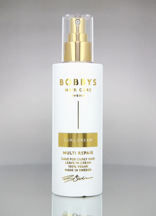 Weiße Flasche mit goldener und schwarzer Schrift, gekennzeichnet 'Bobby's Hair Care', 'Curl Cream' und 'Multi Repair'.
