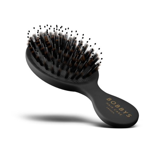 A hairbrush with black handle and grey bristles, some of which have brown hair in them.
