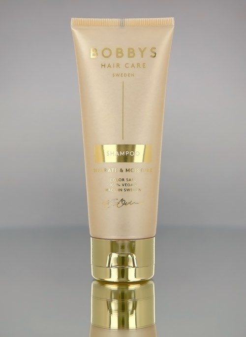 Eine Tube Bobby's Hair Care Shampoo in Gold- und Cremefarben, steht auf einer reflektierenden Oberfläche.