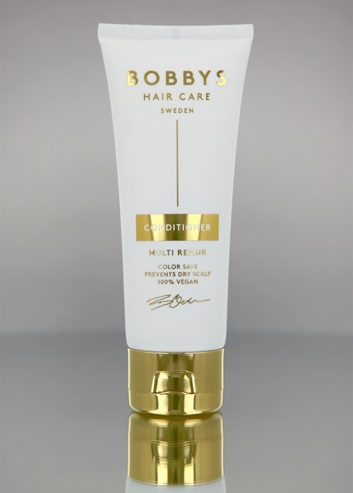 A white tube with gold accents, labeled 'Bobby's Hair Care Conditioner,' stands on a reflective surface.