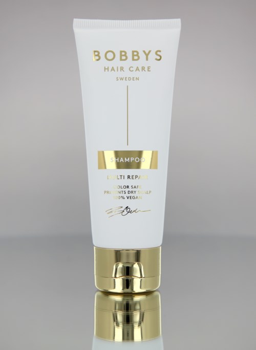 Eine weiße und goldene Tube BOBBY'S Hair Care Shampoo mit goldener Kappe auf grauem Hintergrund.