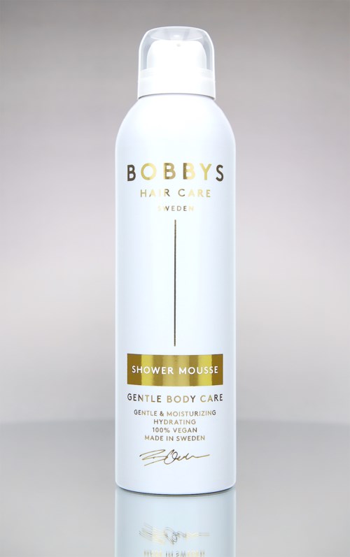 Valkoinen pullo, jossa on kultaiset ja mustat tekstit, nimeltä Bobby's Shower Mousse, hellä kehonhoitoon.