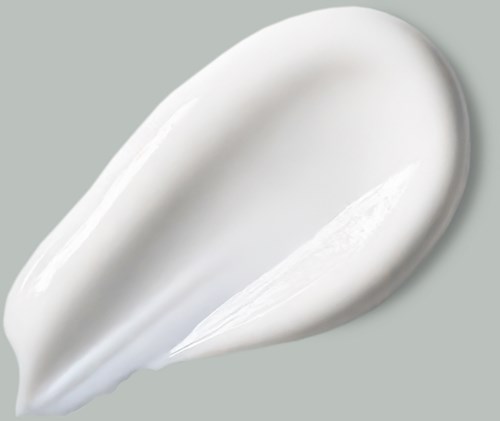 Eine weiße Creme oder Lotion ist auf einer grauen Oberfläche in Tropfenform verteilt.