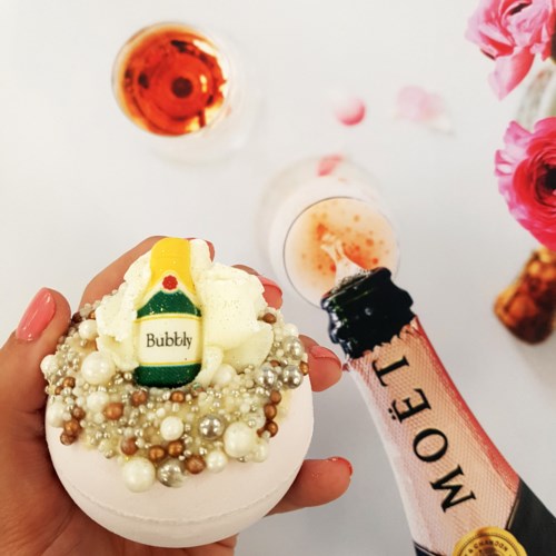 Versierde cupcake met parels, een klein geel detail, omgeven door drankjes en roze bloemen.