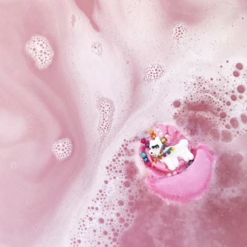 Ein rosa Bad mit Schaum und einem kleinen Einhorn-Spielzeug, umgeben von bunten Perlen.