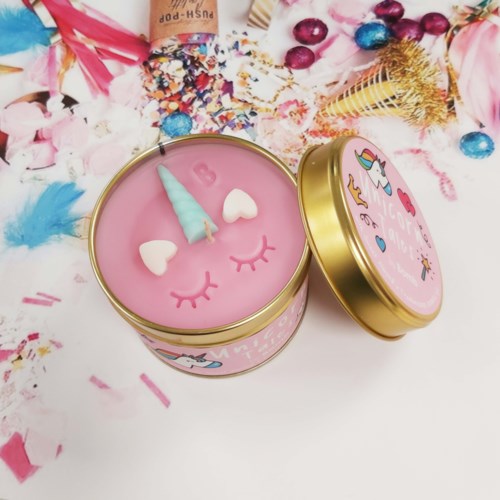 Een roze kaars in blik met een unicorn en regenboog design, omgeven door gekleurde confetti en snoep.