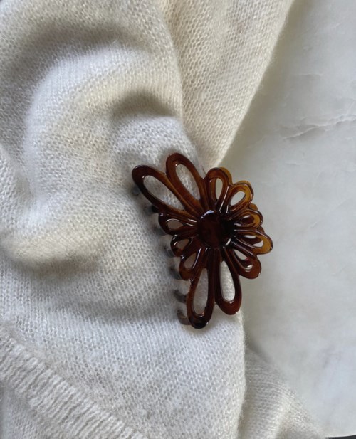 A small brown floral hair clip rests on a white cloth surface.
