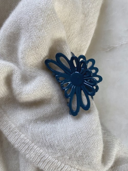 A blue flower-shaped hair clip attached to soft, white fabric.