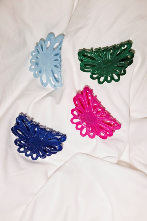 Four colorful plastic hair clips in blue, pink, green, and dark blue placed on white fabric.