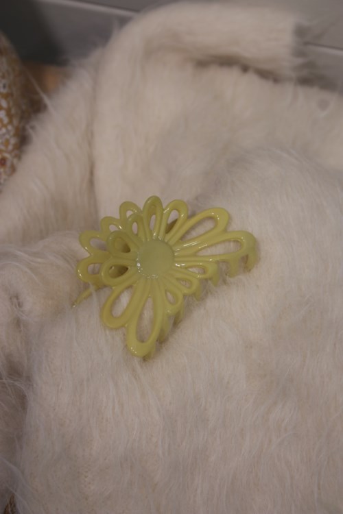 A white animal's back with a yellow plastic butterfly-shaped hair clip. The animal is lying on a soft surface.