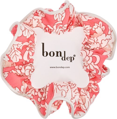 A pink floral scrunchie with a white label that says bon dep and a website address.