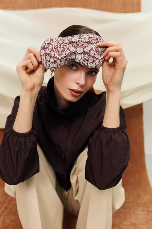 En kvinne poserer med en paisley sittedør på hodet, kledd i en mørk bluse og beige bukser, mot en enkel bakgrunn.