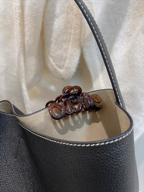 A black bag with a brown decorative element inside, held by a person wearing a light-colored sweater.