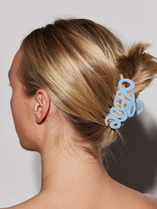 A woman with blonde hair tied back with a large, light blue hair clip shaped like cursive letters.