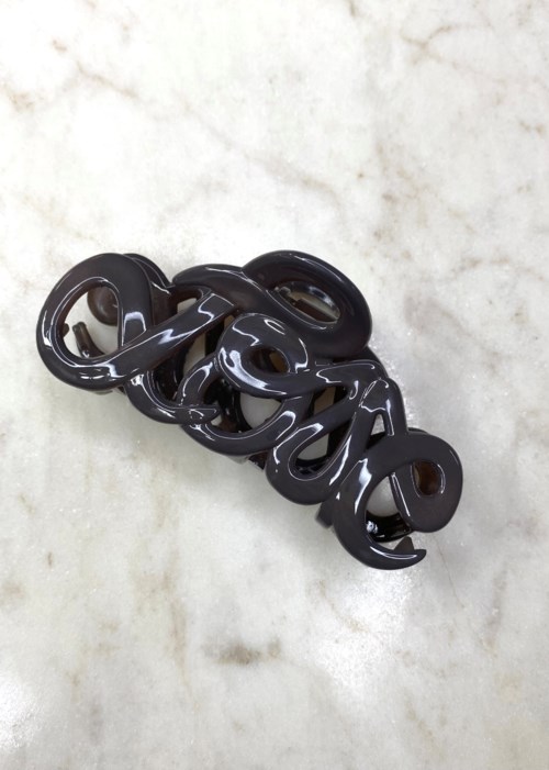 A shiny black decorative object with intertwined loops resting on a light marble surface.