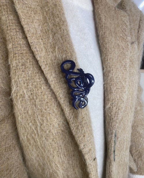 A beige fuzzy coat with a white shirt and a blue decorative pin in the shape of a word.