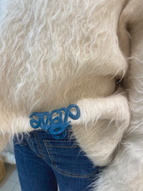 A fluffy white dog with a blue tag on its collar, standing next to a person wearing blue jeans.