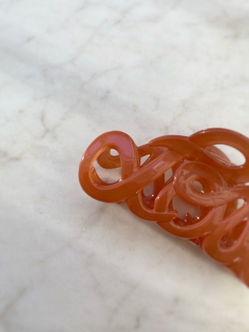A red plastic hair clip with a swirling design, lying on a marble surface.