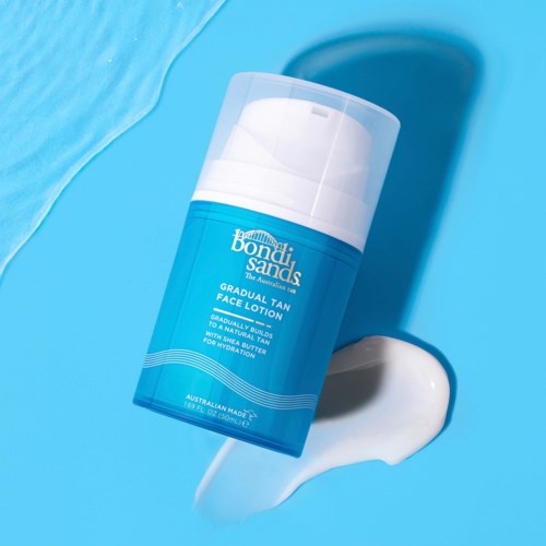 Een blauwe fles Bondi Sands gezichtsbruine lotion met witte pomp, ligt op zijkant met wat lotion ernaast.