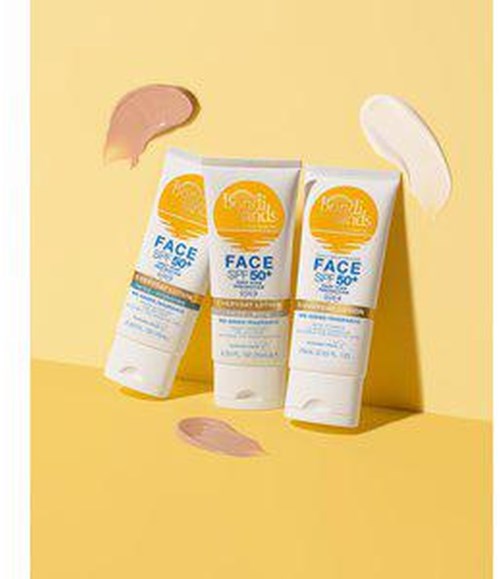 Three tubes of face sunscreen with SPF 50 stand on a yellow background, with dollops of cream nearby.