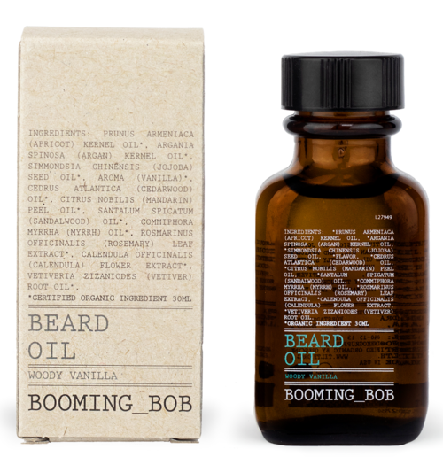 Ein Bartöl-Flasche mit der Aufschrift 'Woody Vanilla' und eine passende Verpackung, die Inhaltsstoffe und den Markennamen 'Booming Bob' zeigt.