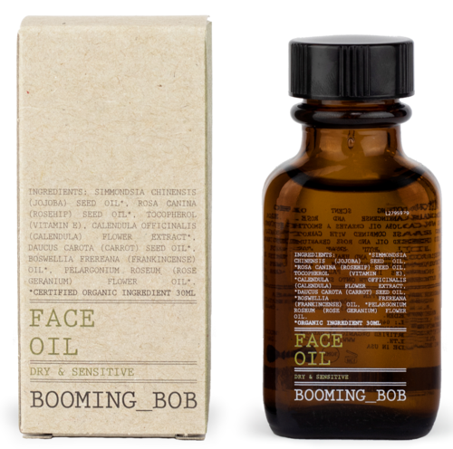 Eine kleine braune Flasche und eine beige Box, beide mit 'Face Oil' für trockene und empfindliche Haut gekennzeichnet, mit Kräuterbestandteilen.