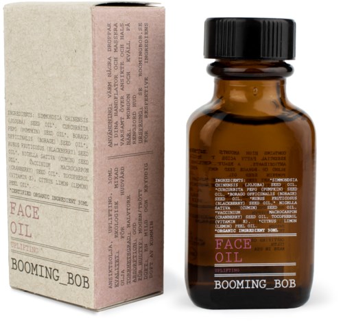 Eine braune Glasflasche mit Beschriftung 'Face Oil' und neben ihr eine rosa-beige Box.