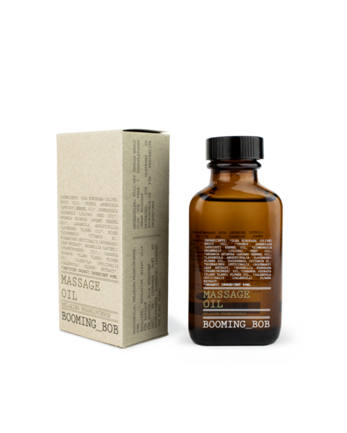 Kleine braune Flasche mit 'Massage Oil' beschriftet neben einer beige Verpackung mit Anweisungen oder Details.