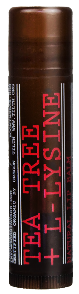 Ein Lippenpflegestift mit der Aufschrift 'Tea Tree + L-Lysine' in Schwarz und Rot. Es steht aufrecht mit braunem Deckel.