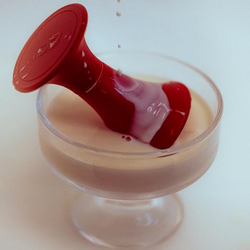 Een rood duikapparaat ligt in een glas met witte vloeistof. Het apparaat is gedeeltelijk ondergedompeld en gekanteld.