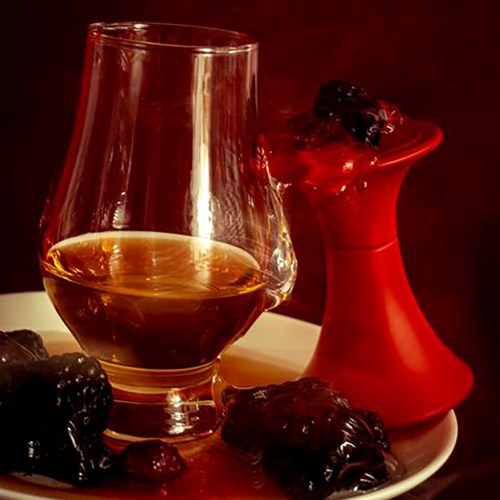 Een glas whisky, zwarte bessen en een rode vaas op een bord met een donkere achtergrond.