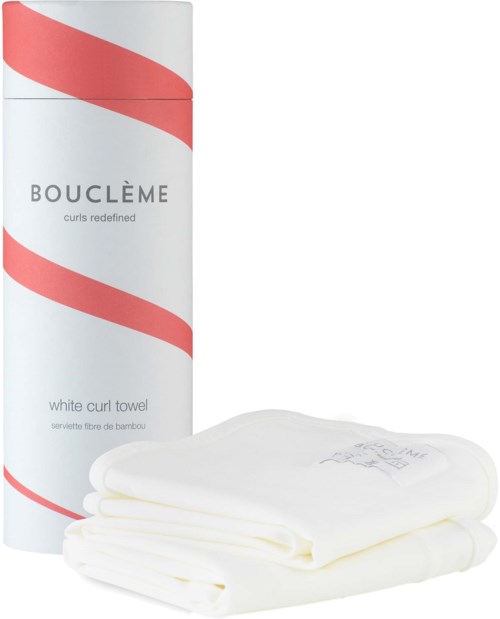 Een hoge cilindervormige container met een rode lus, labeled 'BOUCLÈME' en 'white curl towel,' naast gevouwen witte handdoeken.