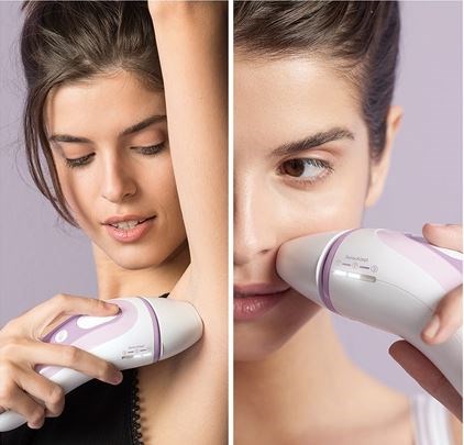 Zwei Frauen verwenden ein Hautgerät, eine hält es unter den Arm, die andere im Gesicht, beide lächeln.