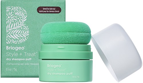 Een groene droogshampoo-puf en container met verpakking op de achtergrond. De doos heeft een bladpatroon en productnaam.