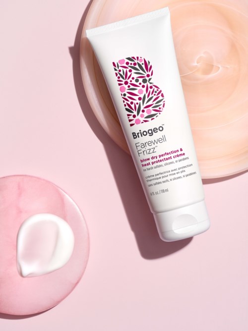 Een witte tube verzorgingscrème met een bloemenlogo, op een roze en perzik achtergrond. Gemarkeerd 'Briogeo Farewell Fizz.'