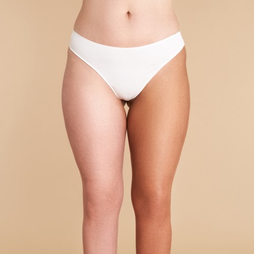 Een persoon met één been donkerder dan de andere, draagt witte ondergoed, staat tegen een beige achtergrond.