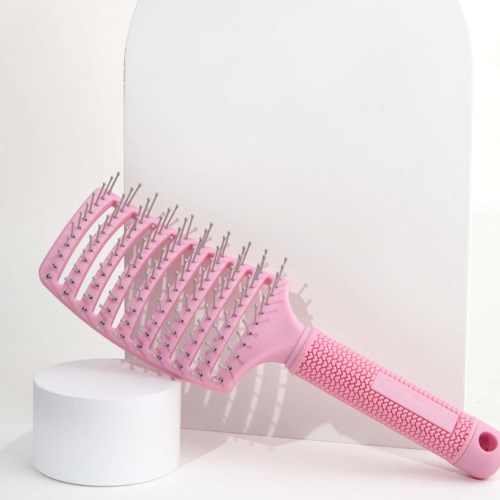 A pink hairbrush with metal bristles leaning against a white backdrop and a small white circle.