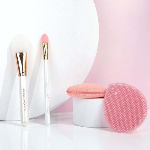 Beauty tools including brushes, a sponge, a cushion, and a silicone facial cleansing brush in pink and white.