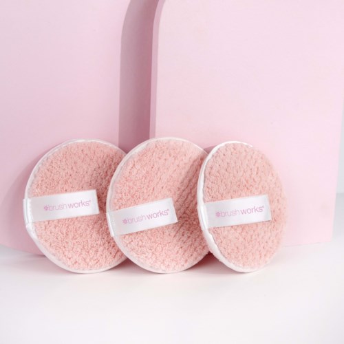 Three pink cleansing pads with white bands labeled "#brush works" are arranged in front of a pink background.