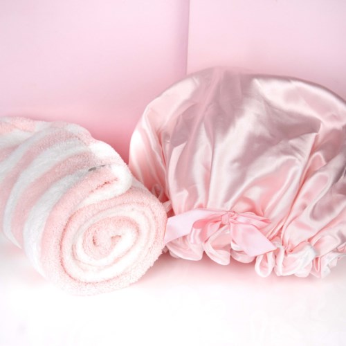 Pink and white striped towel and shiny pink satin bonnet on a pink background.