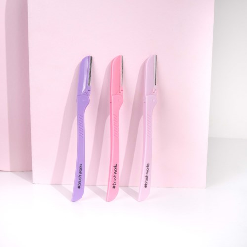 Tre pastellfargede barberhøvler i lilla, rosa og hvit står oppreist på en hvit overflate. De er ordnet med en rosa bakgrunn.