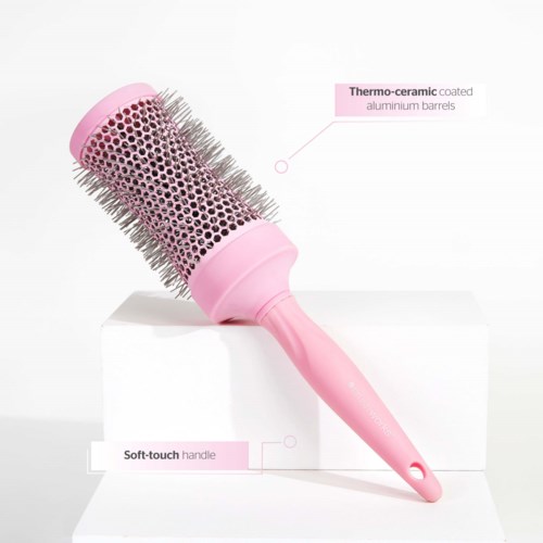 A round hairbrush with a pink handle and plastic bristles, labeled as having thermo-ceramic coated barrels and a soft-touch handle.