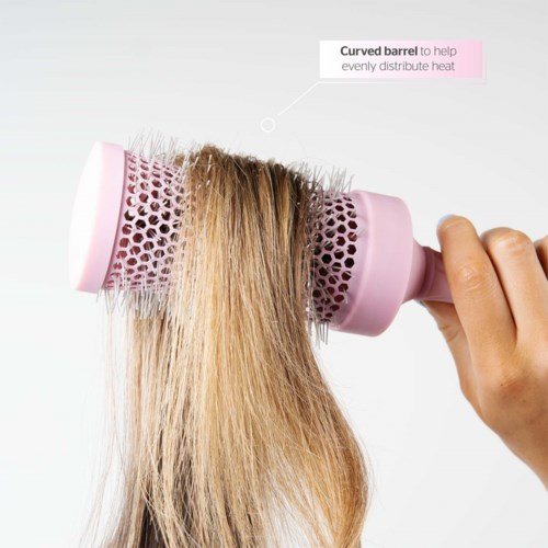 A hand uses a pink round brush with a curved barrel to style hair evenly.