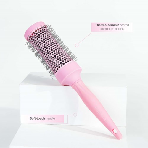 A pink round hairbrush with metal spines, labeled as having a thermo-ceramic coated barrel and a soft-touch handle.