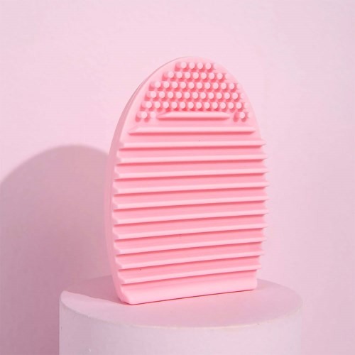 Een roze siliconenborstel met textuurzijde, ovale vorm, op een witte sokkel, met een lichte roze achtergrond.