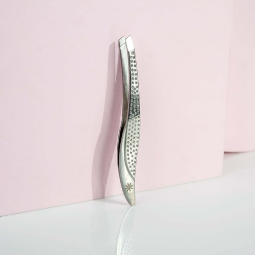 A beauty tweezers stand upright against a pink background, with a reflective surface below.