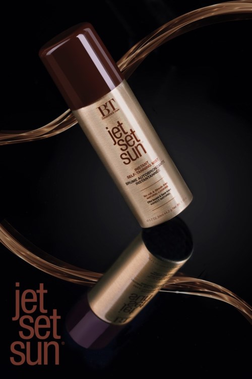 Een beige sprayfles met de tekst 'Jet Set Sun' op een reflecterende zwarte ondergrond met artistieke bruine lijnen.